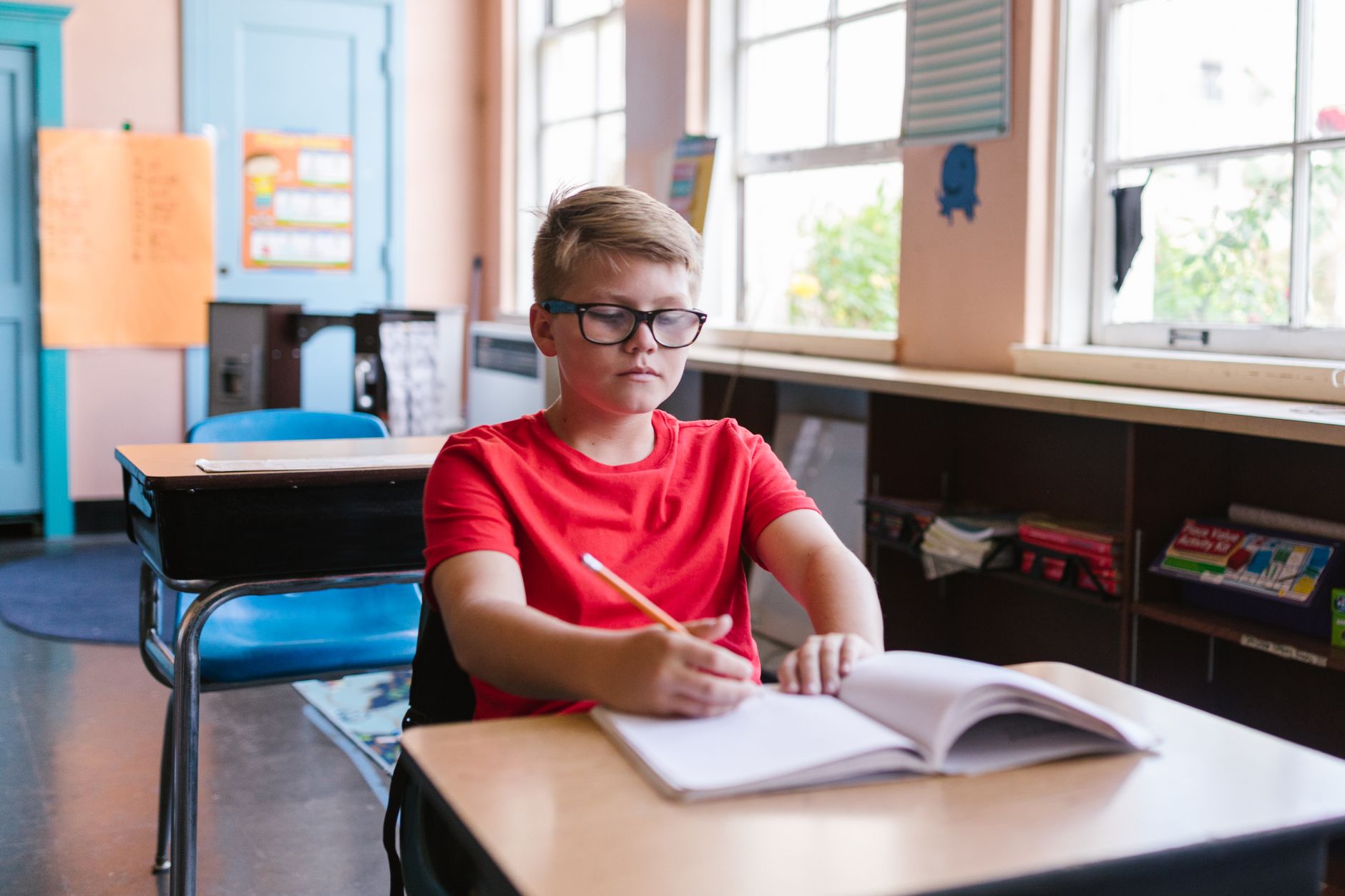 Boy in a classroom writing in notebook, focused on assignment at desk.