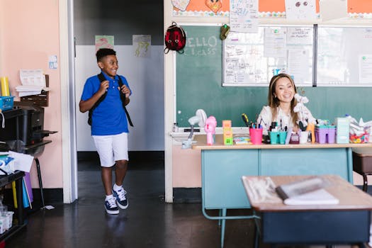 A cheerful student enters the classroom where a teacher is seated at a desk, ready for class.