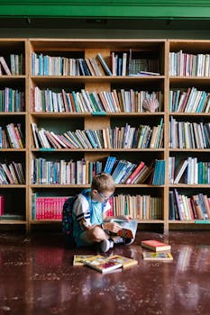 A young boy sitting on the floor reading a book in a library environment.