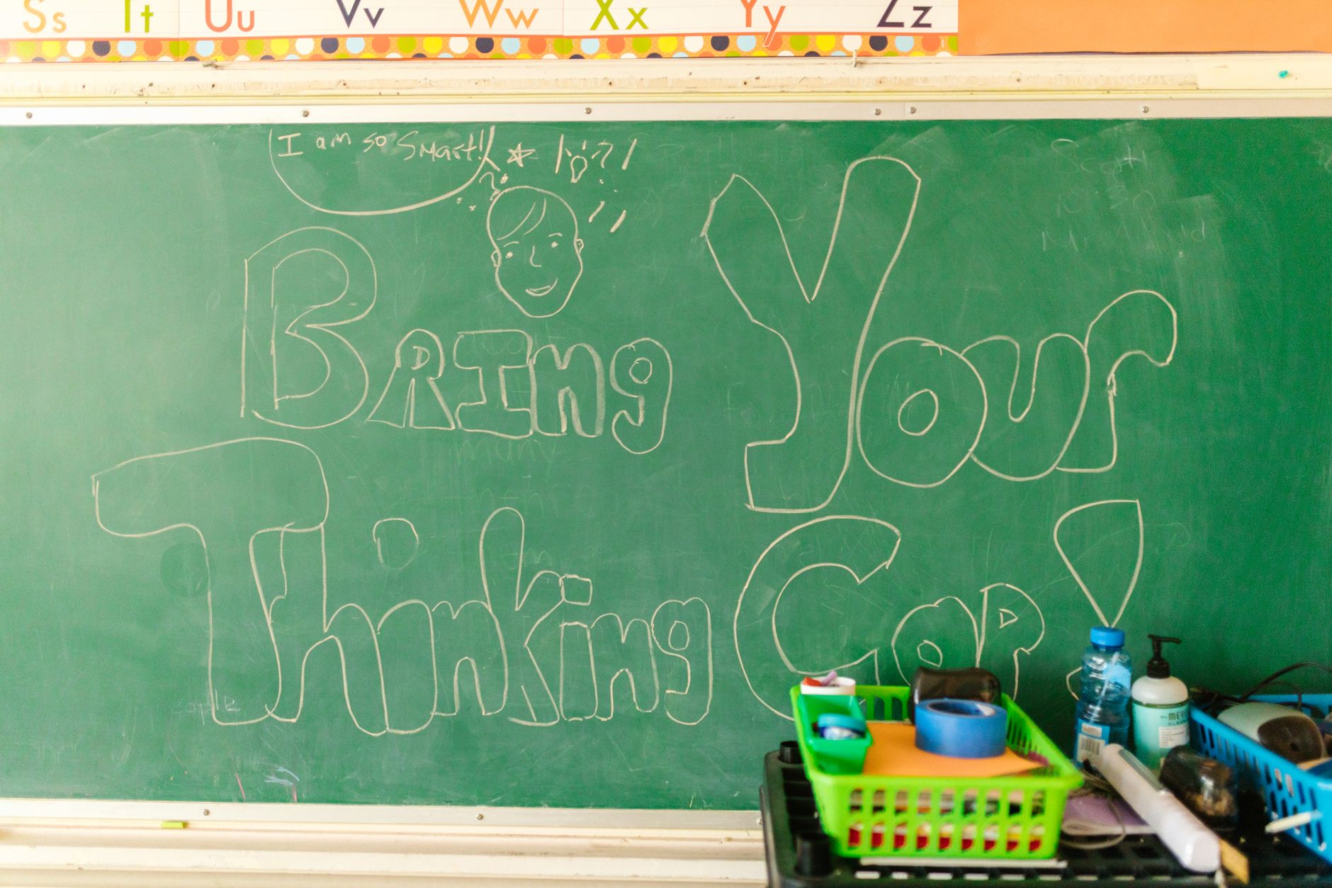 Classroom scene with chalkboard message "Bring Your Thinking Cap" and supplies.