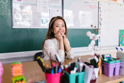 Cheerful teacher sitting at a desk in a bright classroom with school supplies.