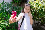 A Girl in White Dress Carrying Backpack while Taking a Selfie