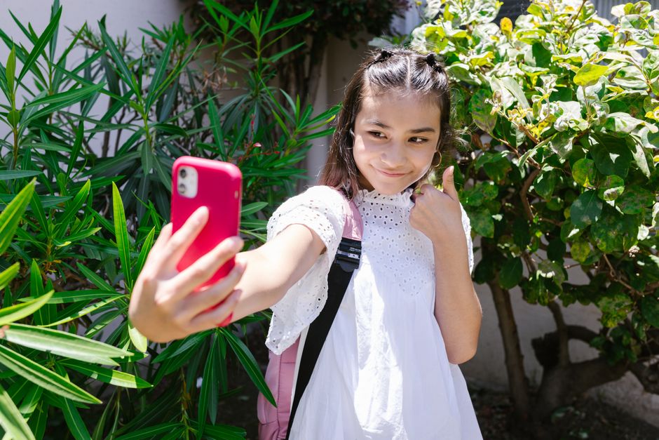 A young girl takes a selfie outside, capturing her excitement on a sunny day.