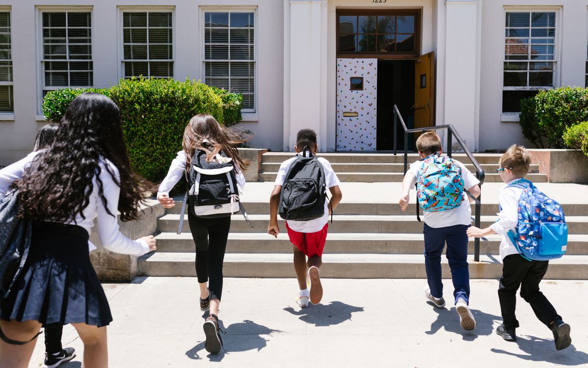 Group of students with backpacks running into school, captured from behind, showing excitement.