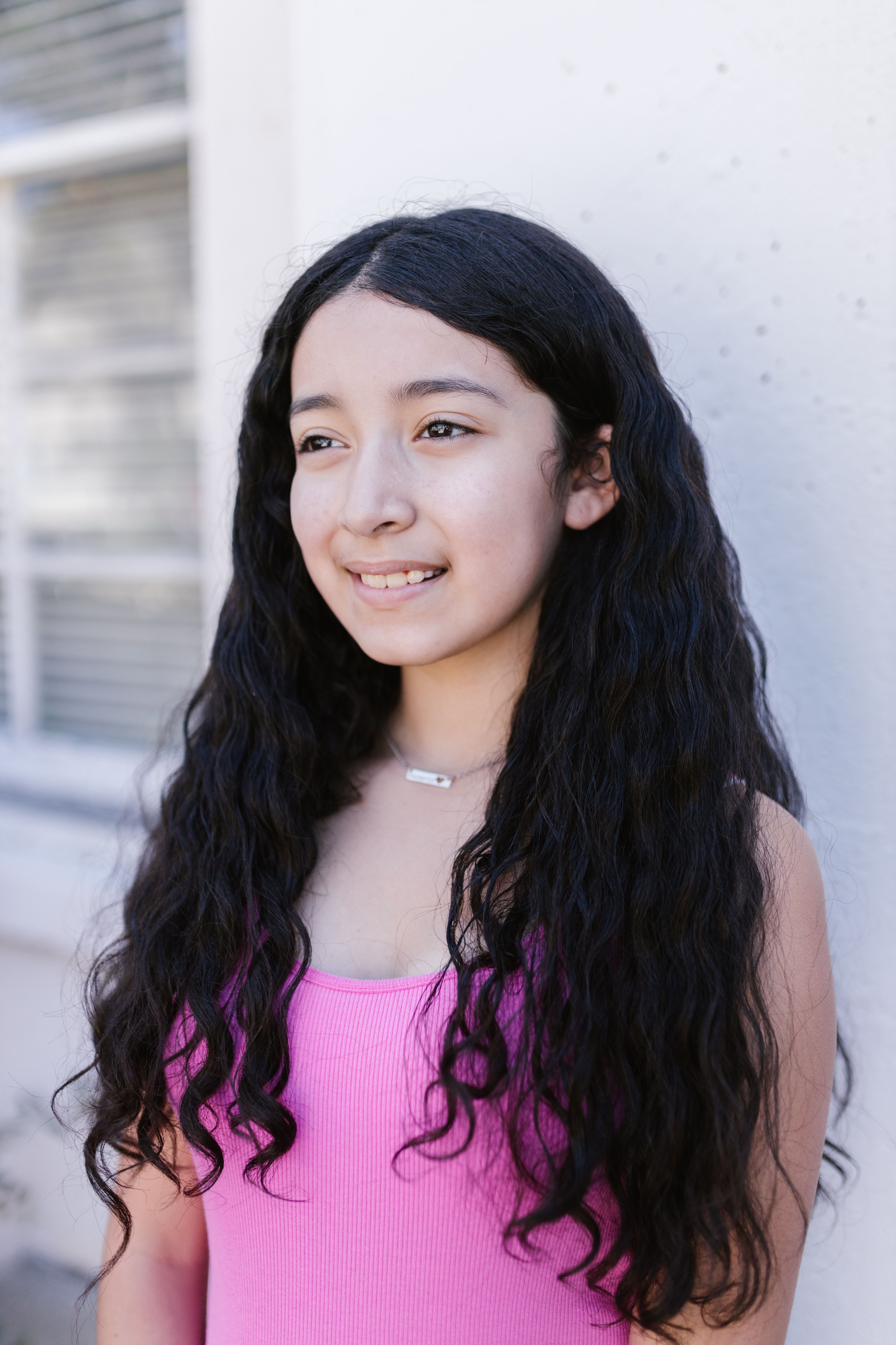 Portrait of a young girl in a pink tank top, smiling outdoors.