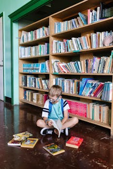 A child enjoys reading books inside a library, surrounded by shelves.