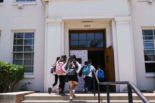 Free Group of students with backpacks entering a school building. Perfect for back-to-school themes. Stock Photo