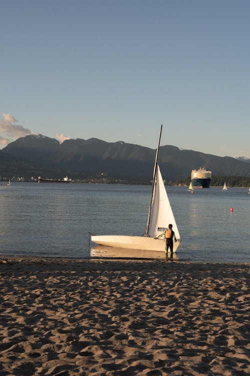 Man Standing Beside His Sailboat on Water