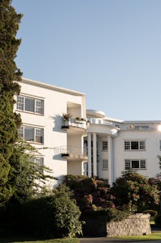 A beautifully lit white apartment building surrounded by greenery under a clear blue sky.