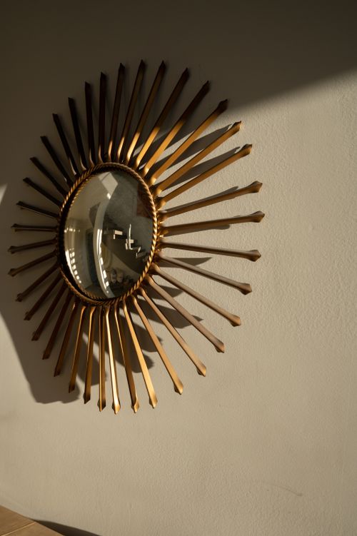 Free Stylish sunburst mirror with golden frame casting shadows on a wall. Stock Photo
