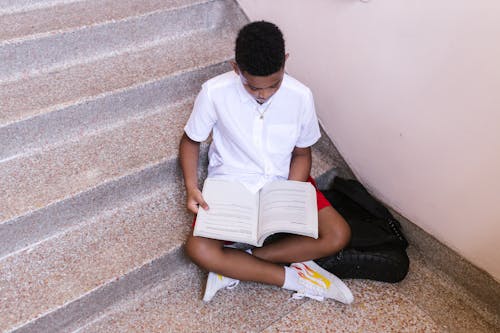 A Boy Sitting on Concrete Stairs Reading a Book