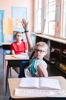 Two young boys in an elementary classroom raising hands, actively participating in learning.