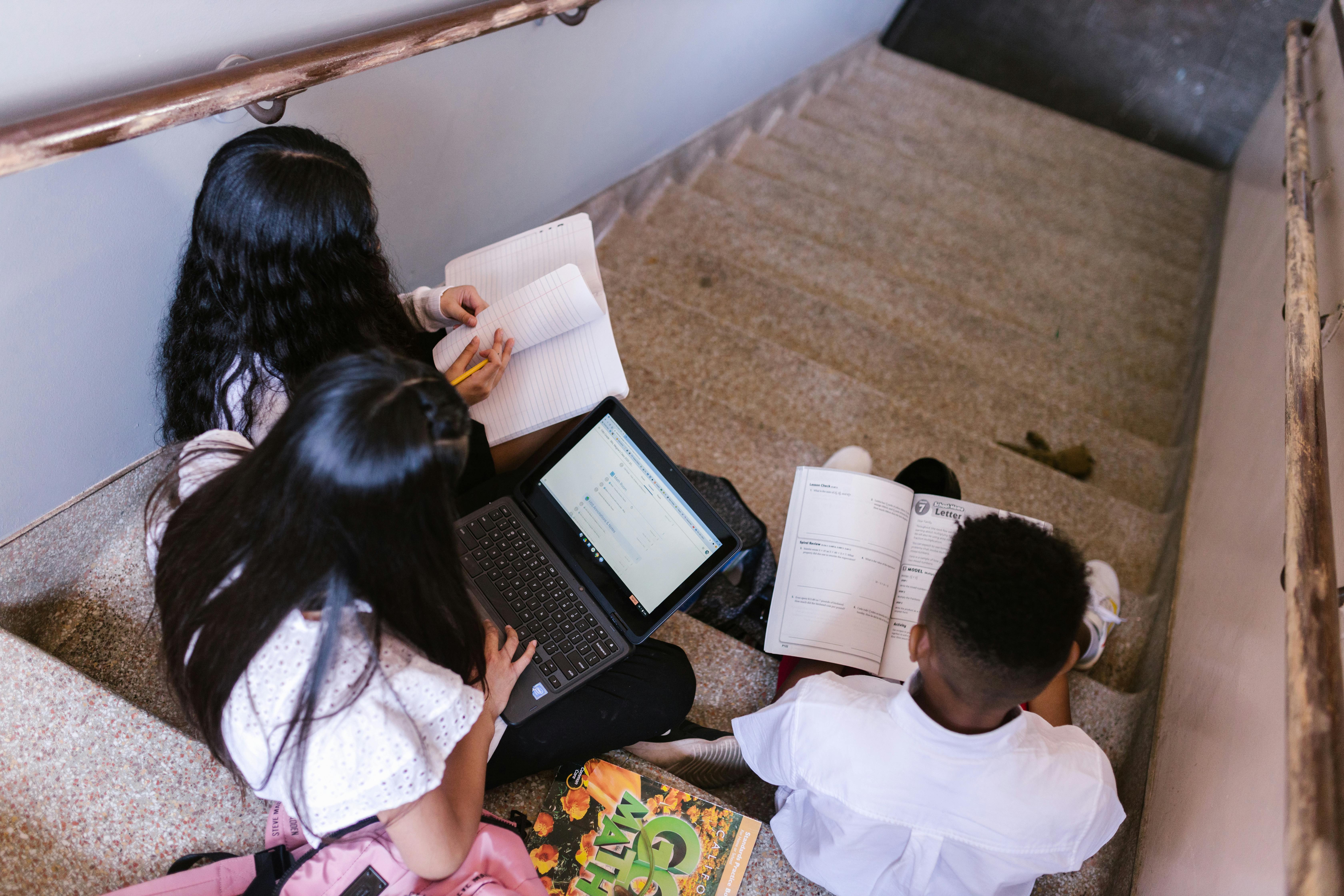 children sitting on stairs holding books and laptop