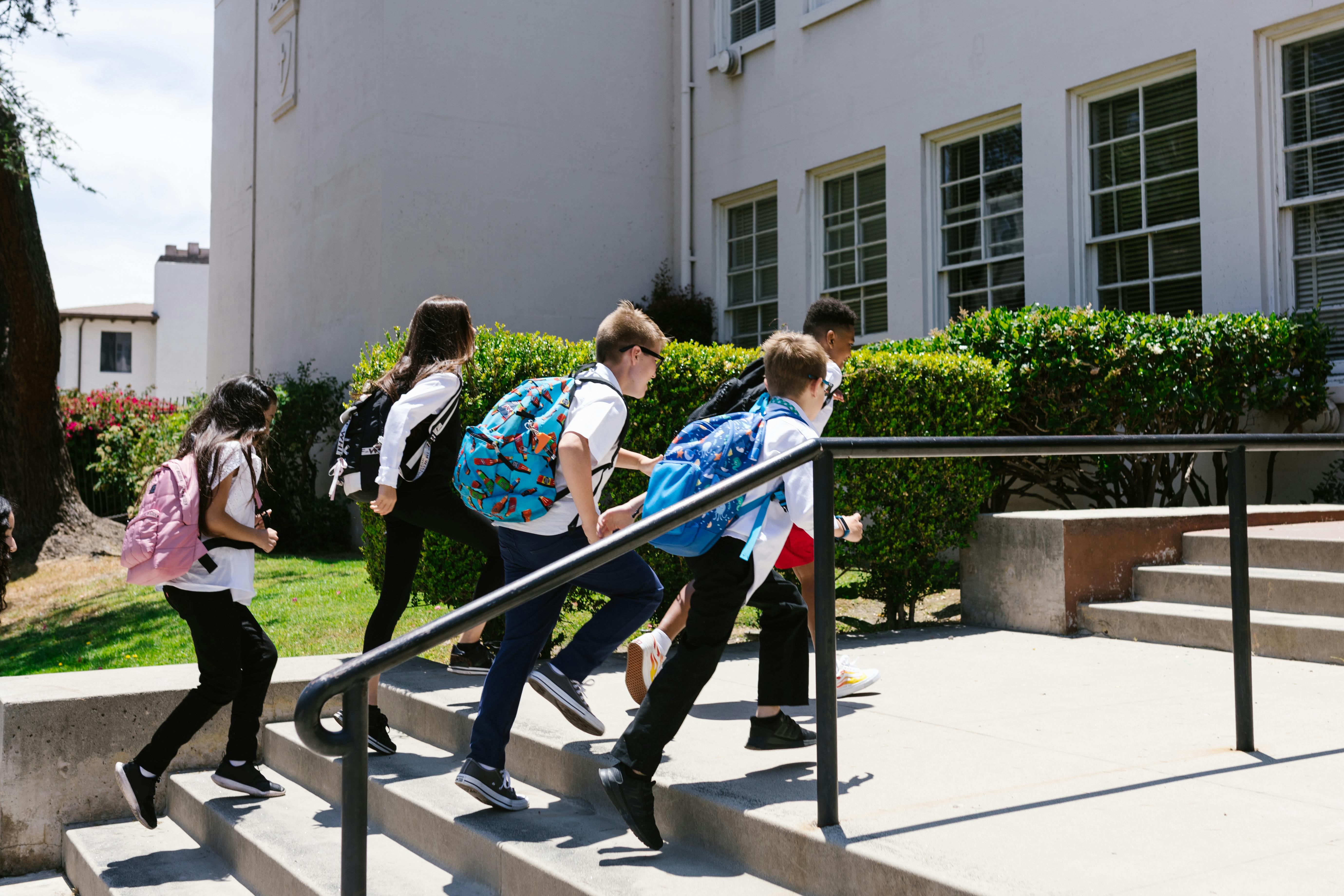Children joyfully running up steps to school, backpacks in tow, showcasing school life.