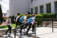 Children joyfully running up steps to school, backpacks in tow, showcasing school life.