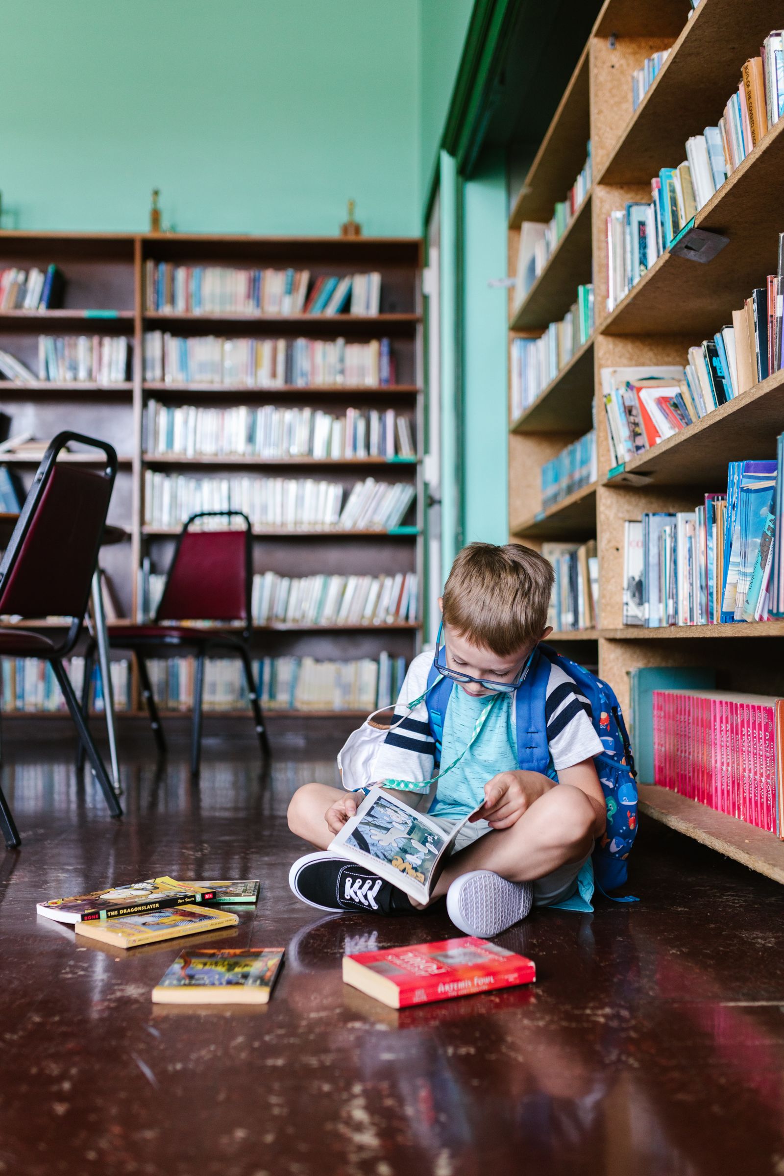 Хлопчик в окулярах читає книжку в бібліотеці