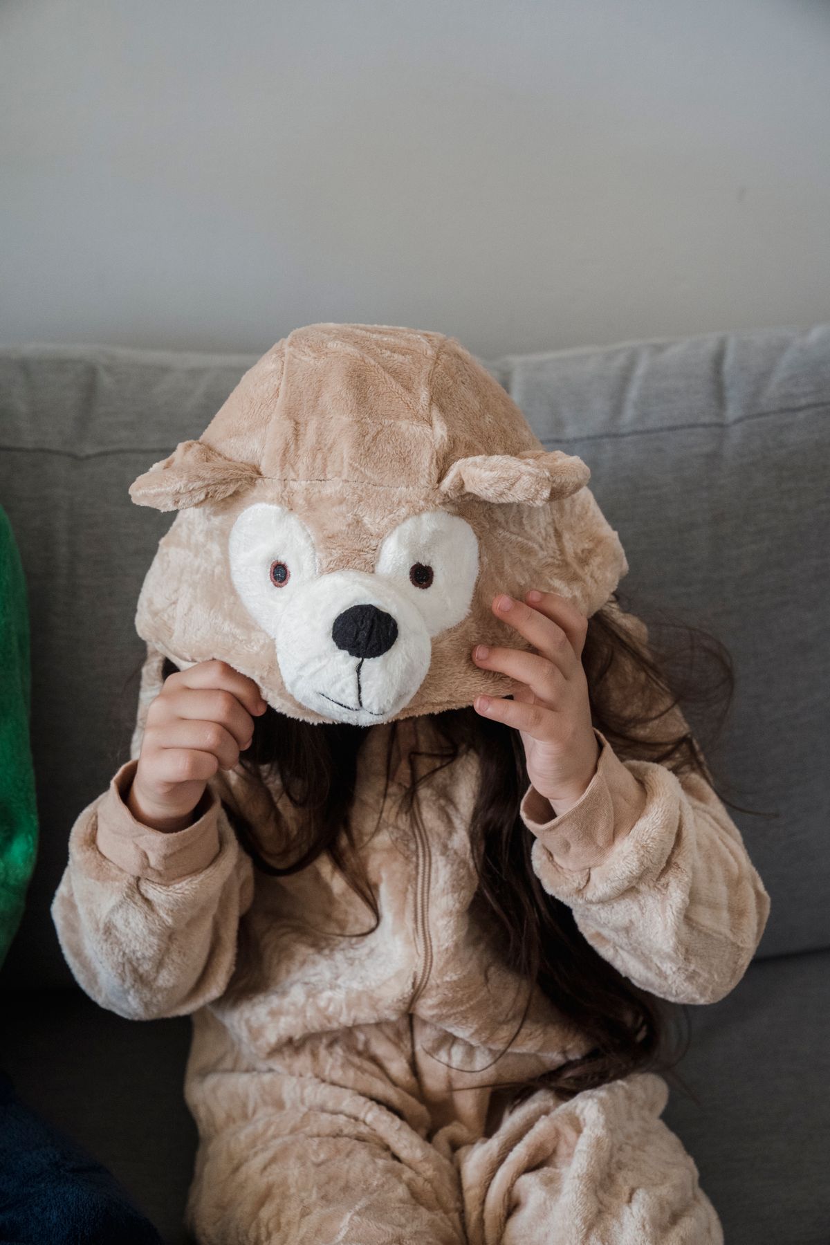 Child in an animal bear hoodie sitting on a sofa at home