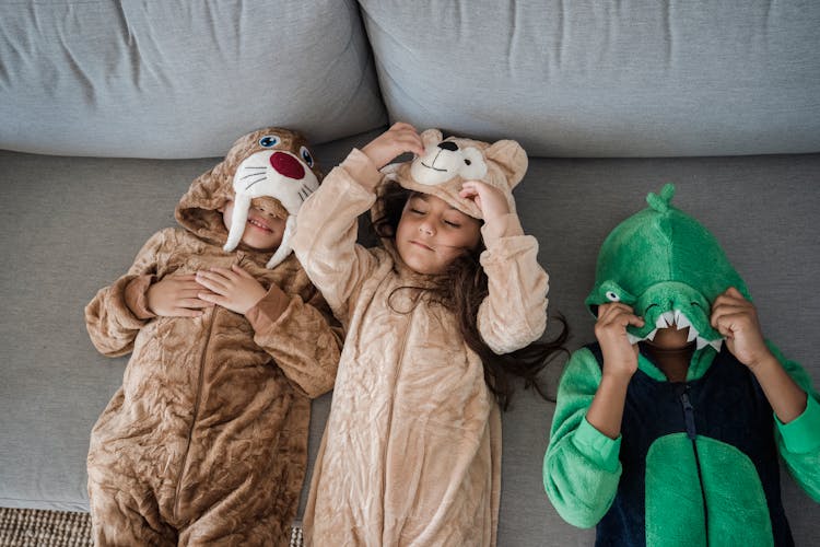 Three Kids In Animal Costumes Lying On Grey Sofa