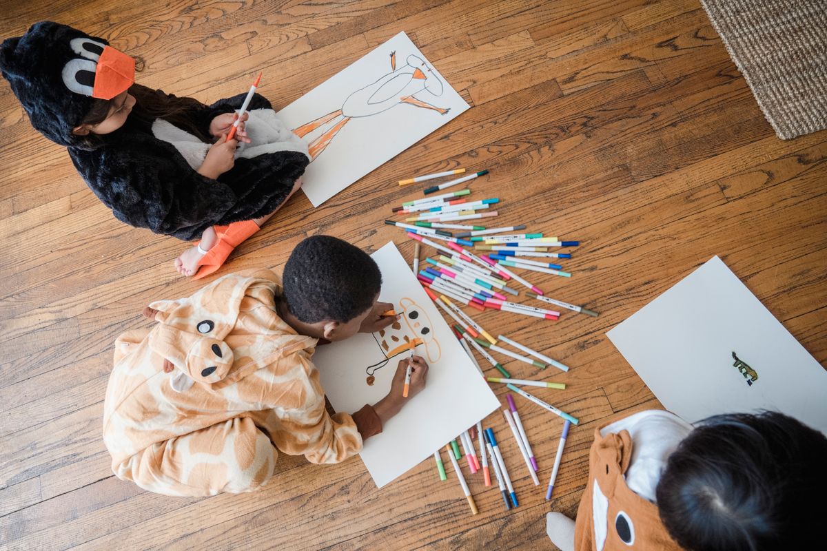 Kids in animal costumes lying on a wooden floor drawing a koala with markers
