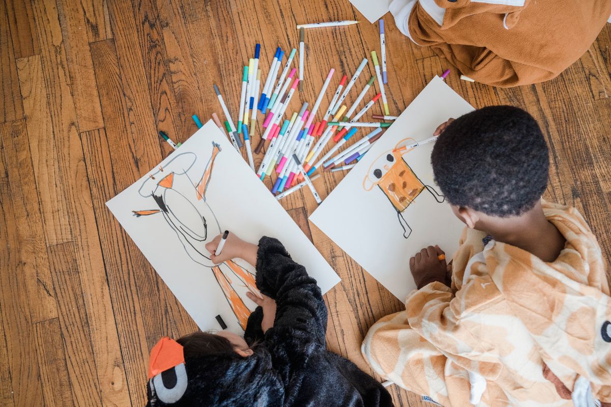 Kids in animal costumes coloring a friendly dinosaur picture on the floor