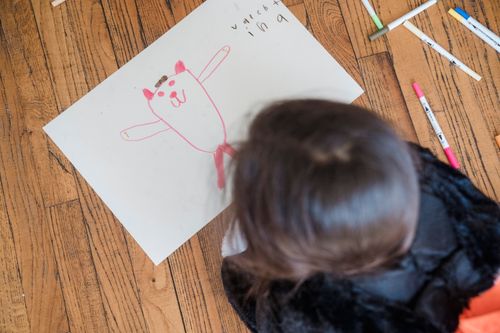 Free A young child draws on paper with crayons on a wooden floor. Creative playtime. Stock Photo
