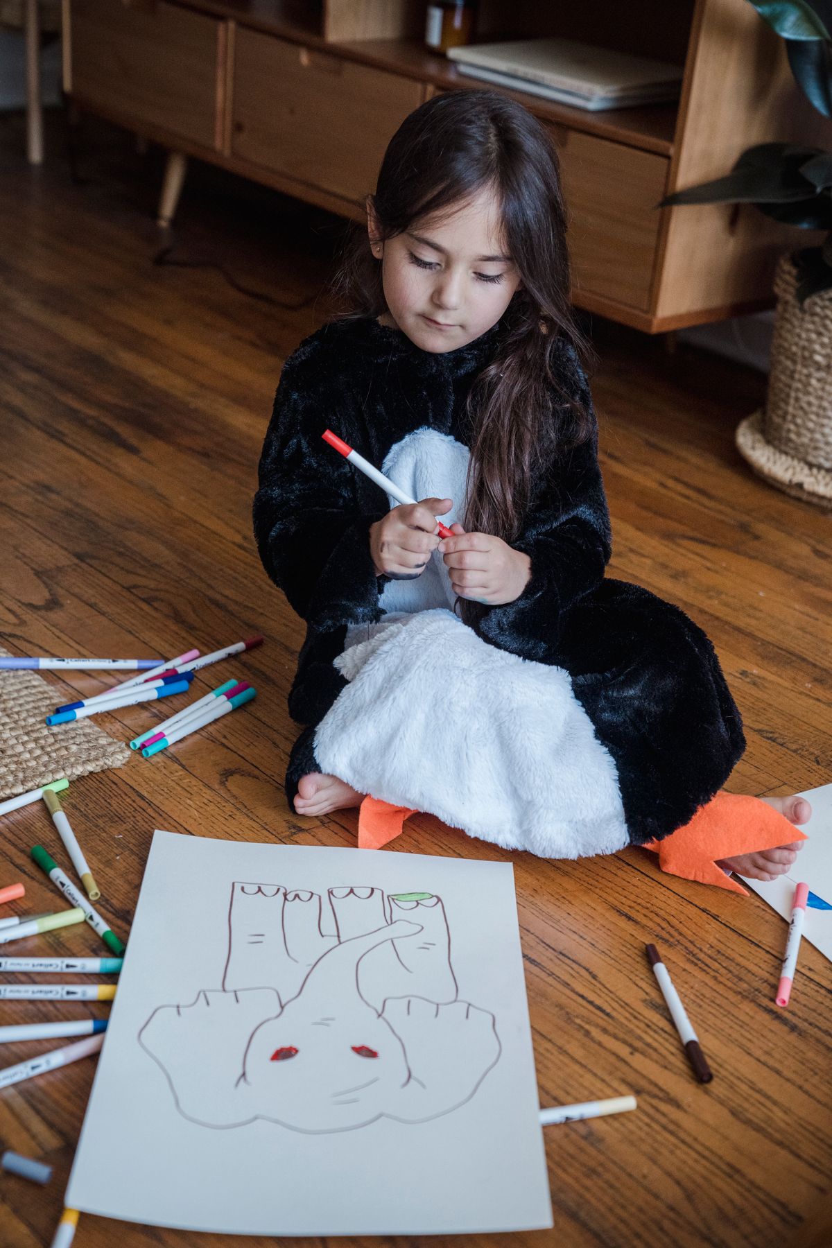 Young girl in a penguin costume drawing with markers indoors