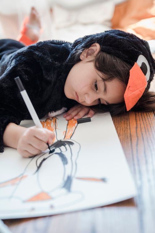 Free Young girl in animal costume creatively drawing on paper indoors. Stock Photo