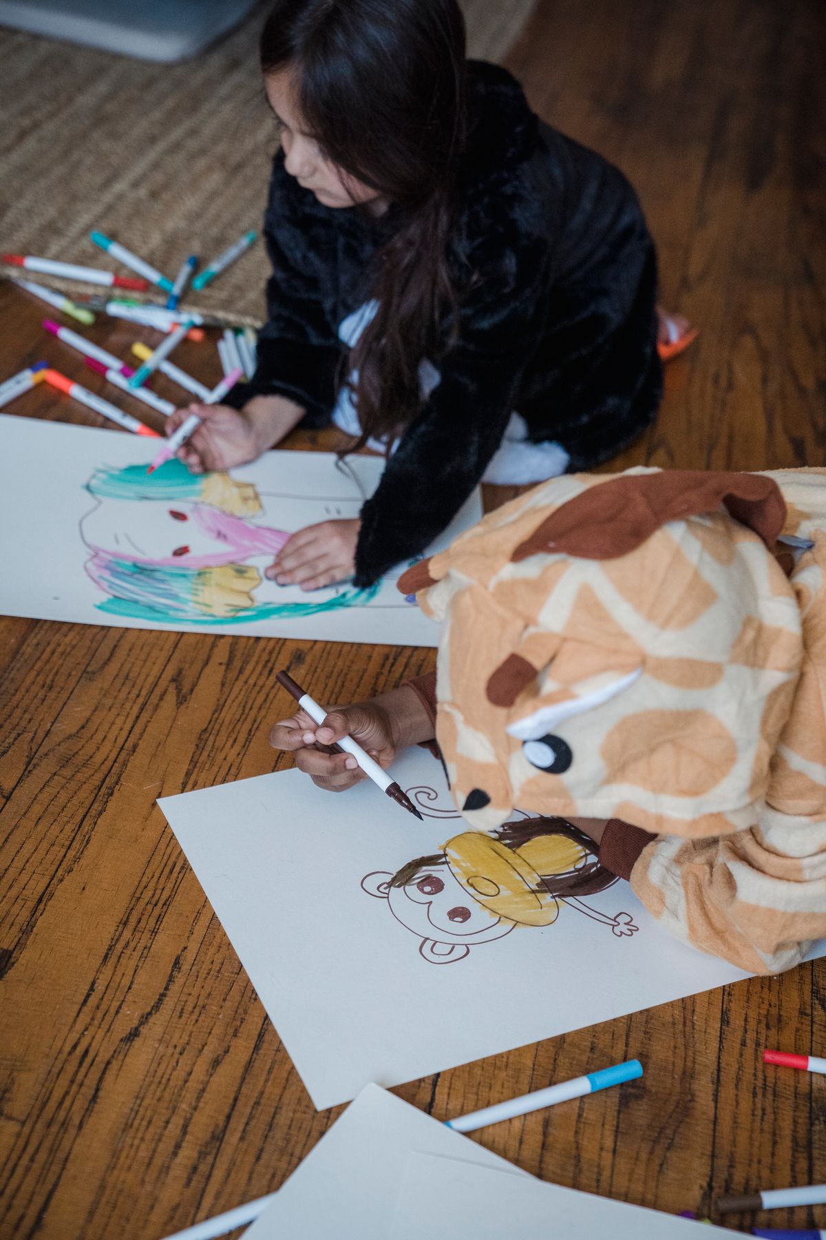Kids in animal costumes drawing a cow with markers on a wooden floor