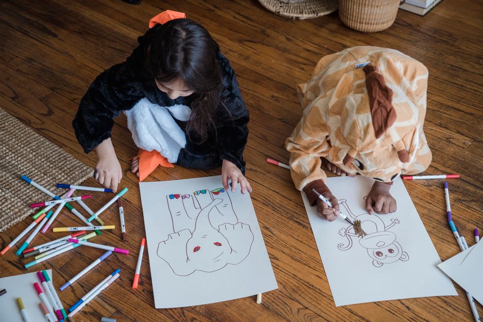 Children in animal costumes drawing on paper with colorful markers indoors.