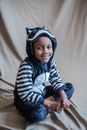 A Kid in Animal Costume Sitting on a Beige Fabric while Smiling at the Camera