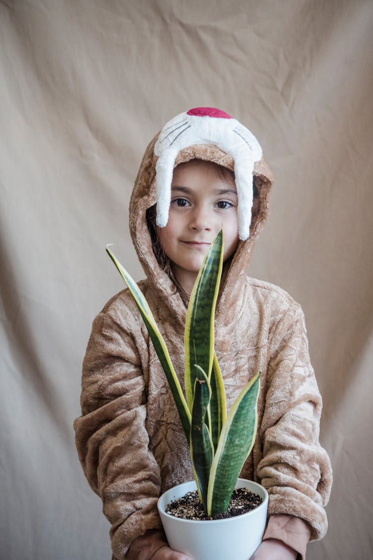 Kid Wearing Animal Costume While Holding A Potted Green Plant