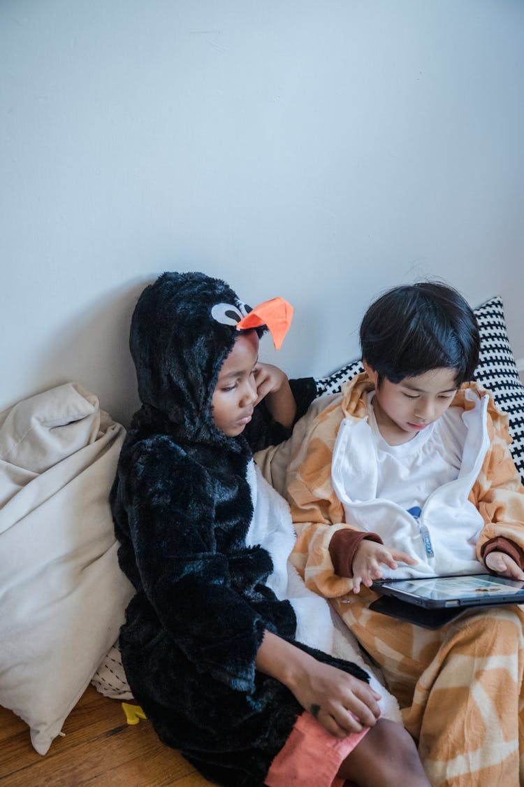 Kids Wearing Animal Costume Sitting On A Wooden Surface While Looking At The Screen Of A Tablet