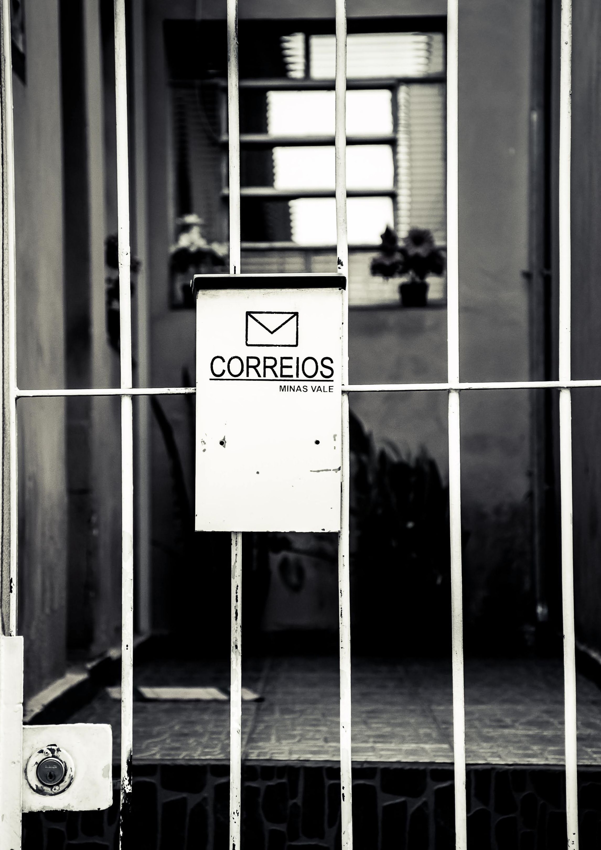 Black and white image of a Correios mailbox behind a metal gate in Brazil.