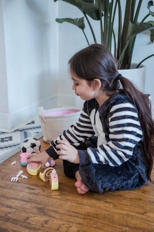 A Girl Sitting on a Wooden Flooring while Playing Toys