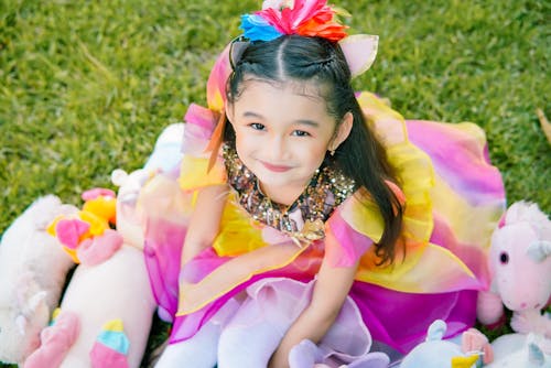 A Girl Wearing Colorful Dress Sitting on a Grass Field while Smiling at the Camera