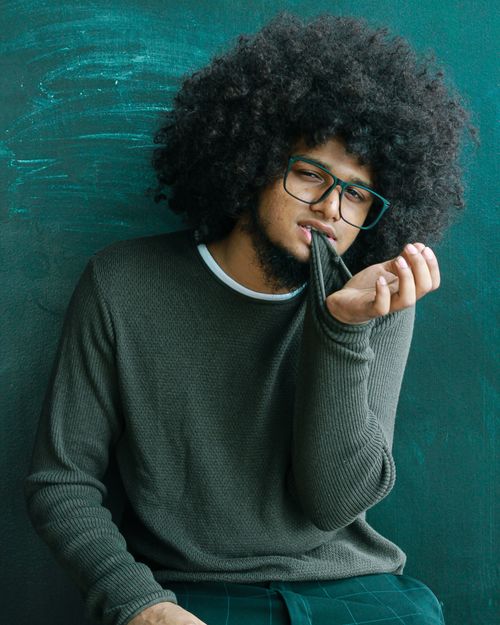 Free Portrait of a young man with afro hairstyle in a classroom setting, wearing eyeglasses. Stock Photo