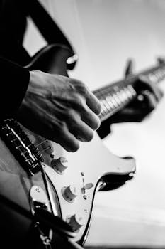 Black and white photo of a musician's hand strumming an electric guitar.