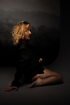 Elegant portrait of a woman sitting gracefully in a dark, moody studio environment.