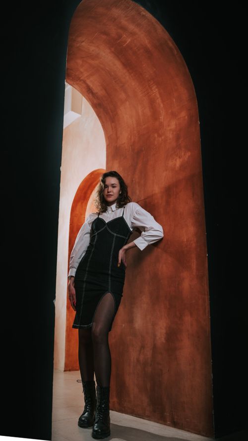 Free Fashionable woman wearing a black dress poses elegantly by an artistic archway indoors. Stock Photo