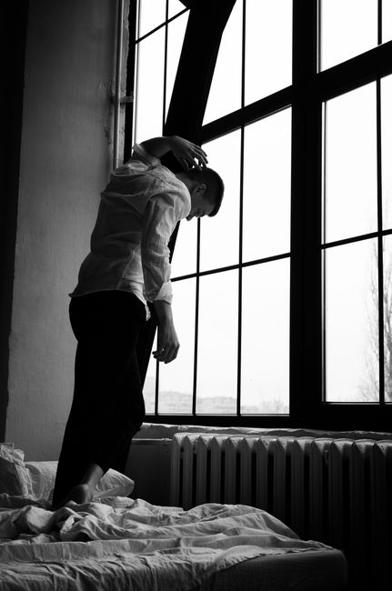 Artistic black and white photo of a person gazing out a window, creating a reflective mood.