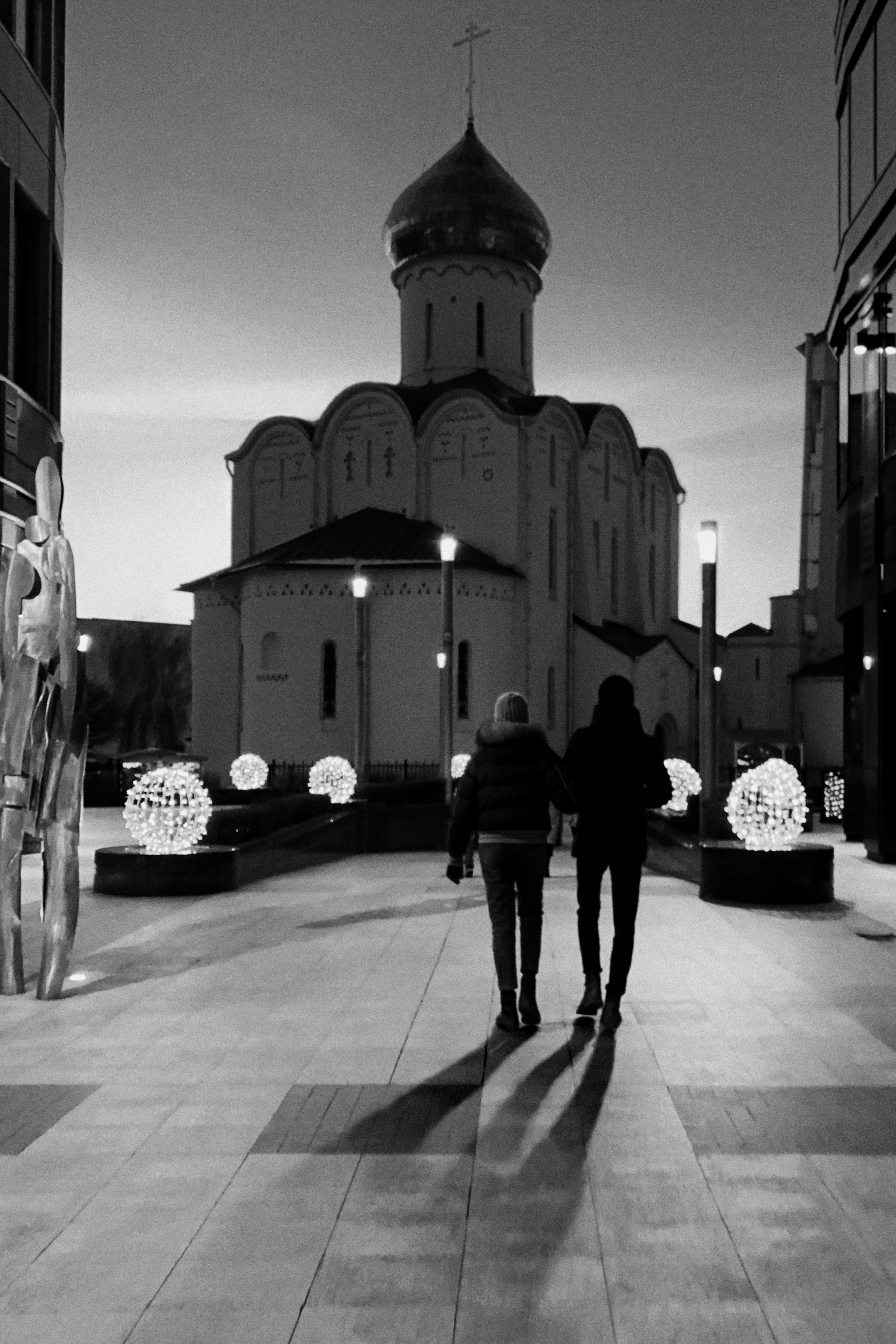 Two people walking towards a church in Moscow, captured in black and white, offering a serene winter evening scene.