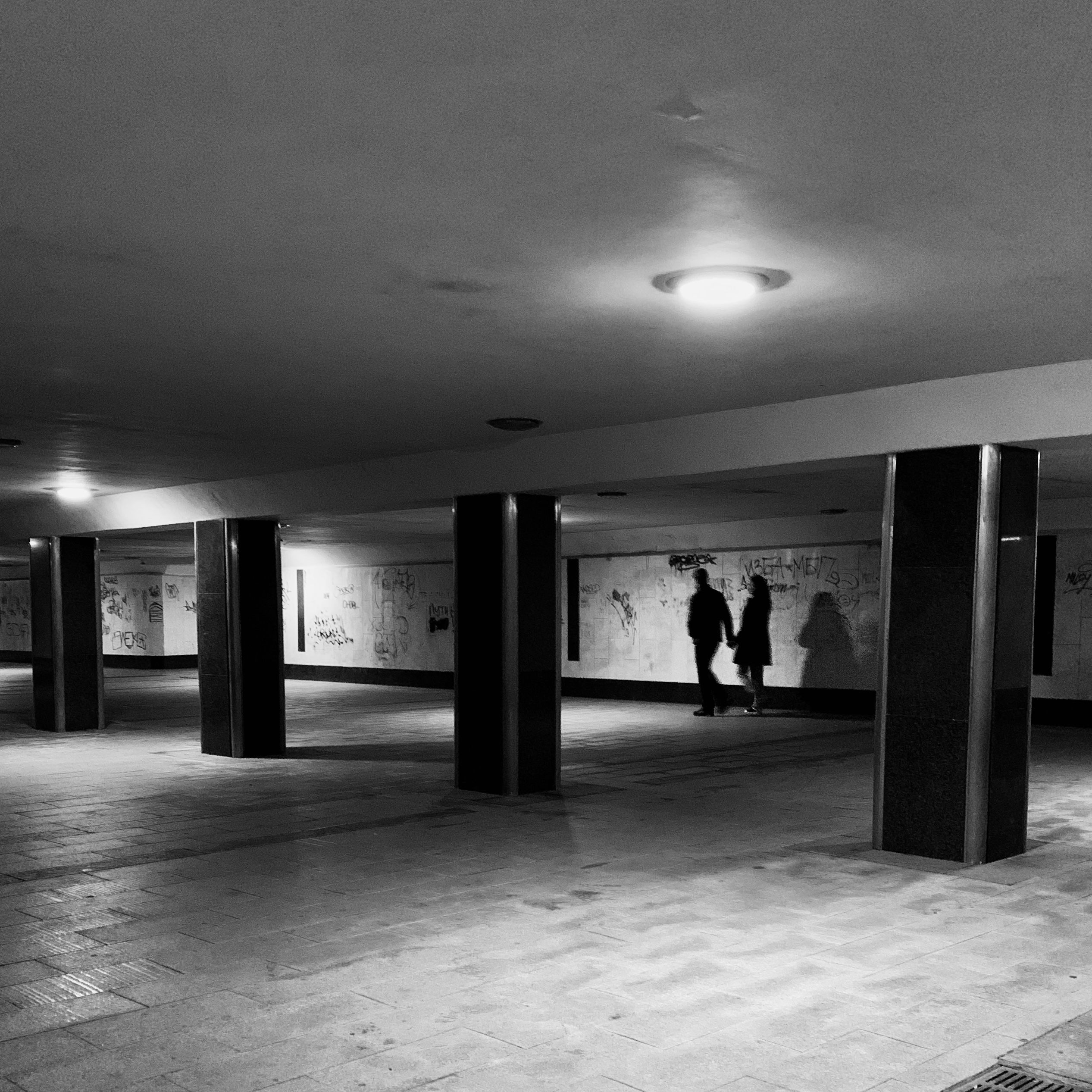 Silhouetted figures walking in an underground hallway, creating a dramatic shadow effect.