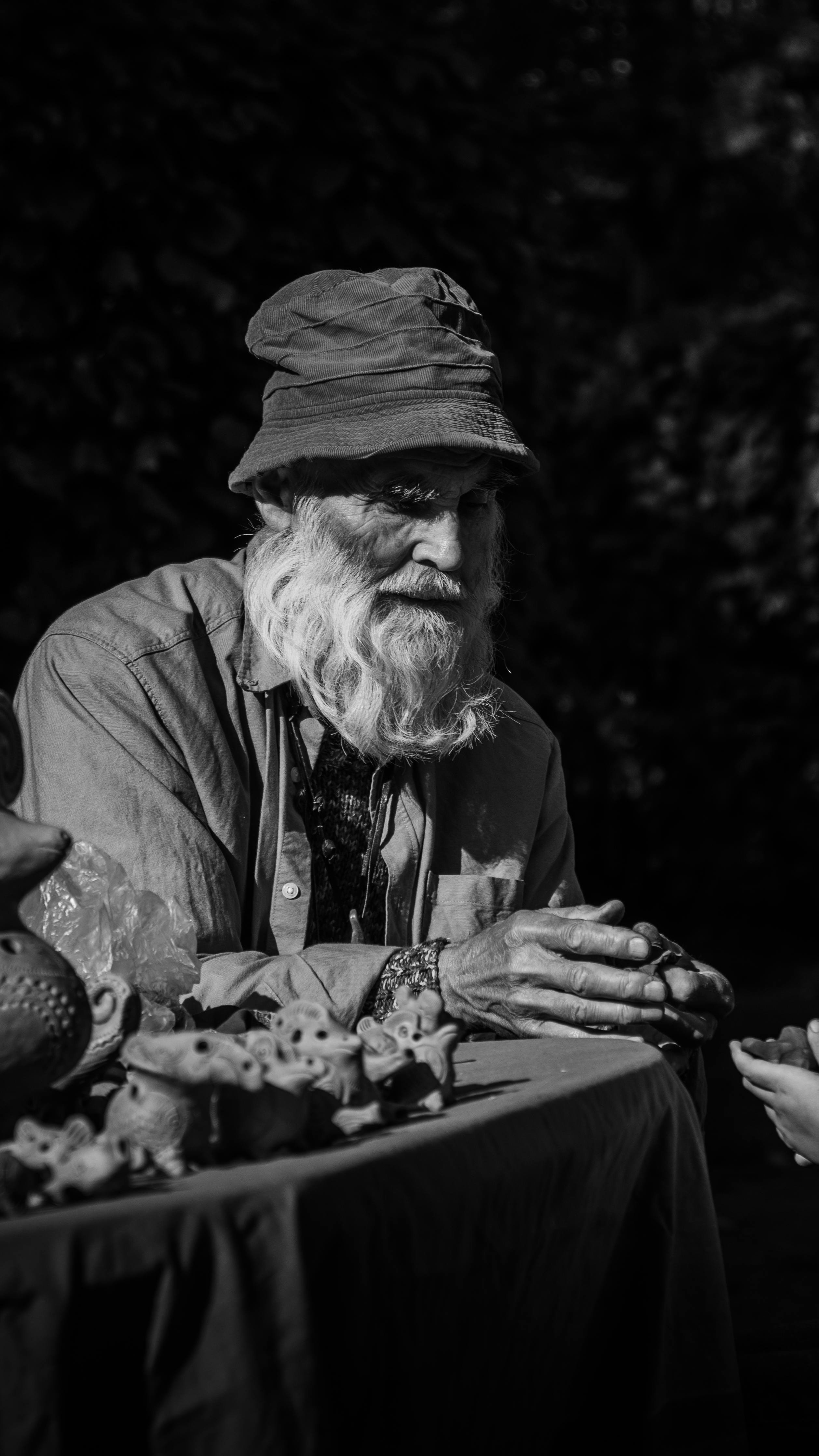 Black and white photo of an elderly man with a beard and bucket hat at an outdoor market.