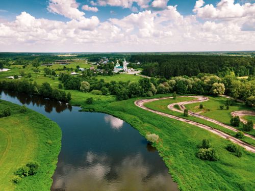 Free A stunning aerial view of a river winding through vibrant countryside with a distant village. Stock Photo