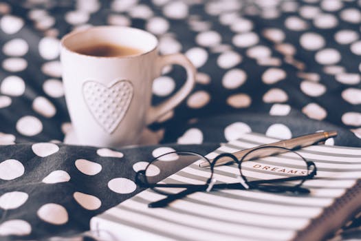 Relaxing morning scene with a hot coffee, dream journal, and eyeglasses on a stylish polka dot bedspread.
