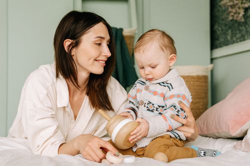 Free A loving mother and toddler share a playful moment indoors, focusing on a wooden toy. Stock Photo