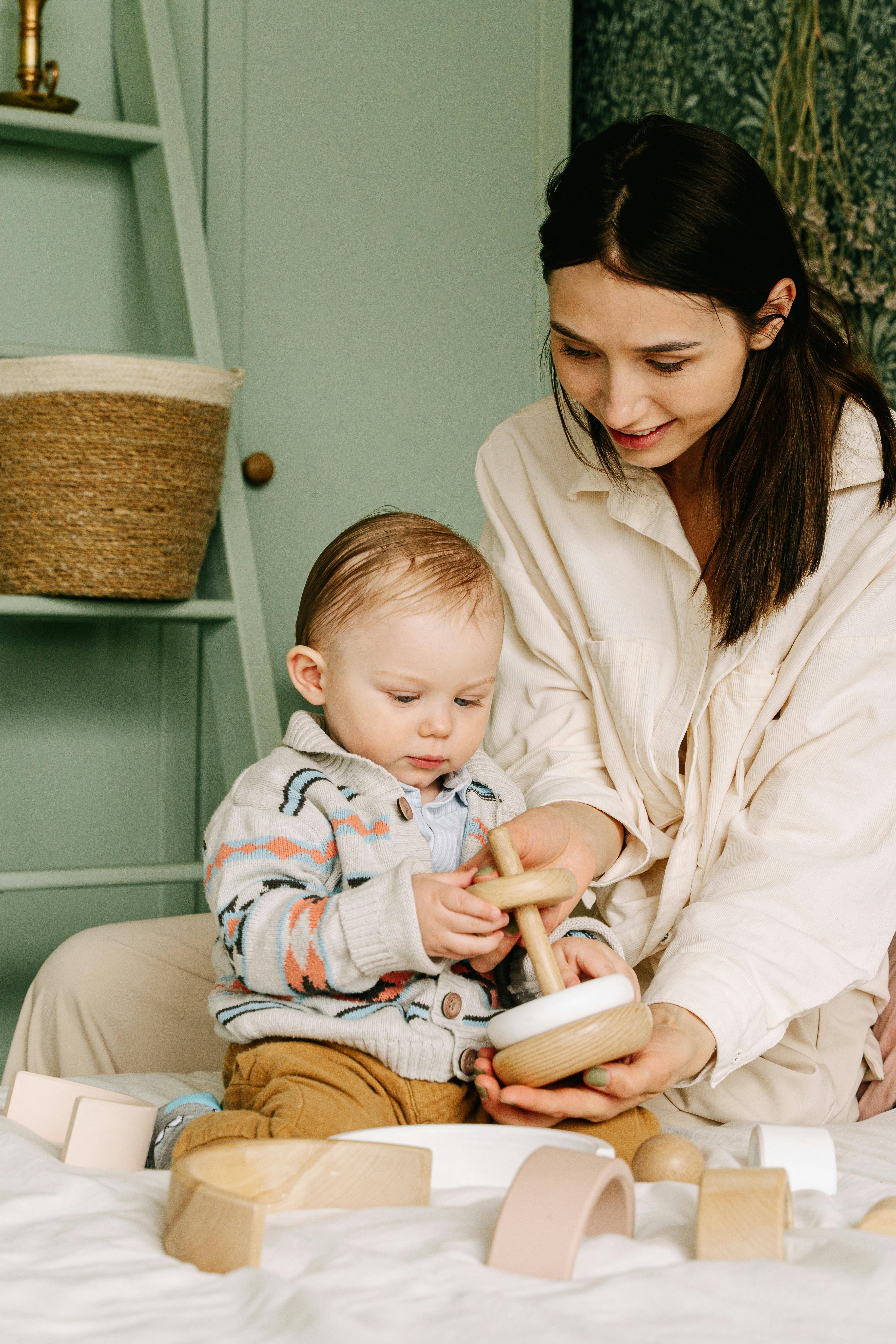 baby boy playing with wooden toy beside a woman