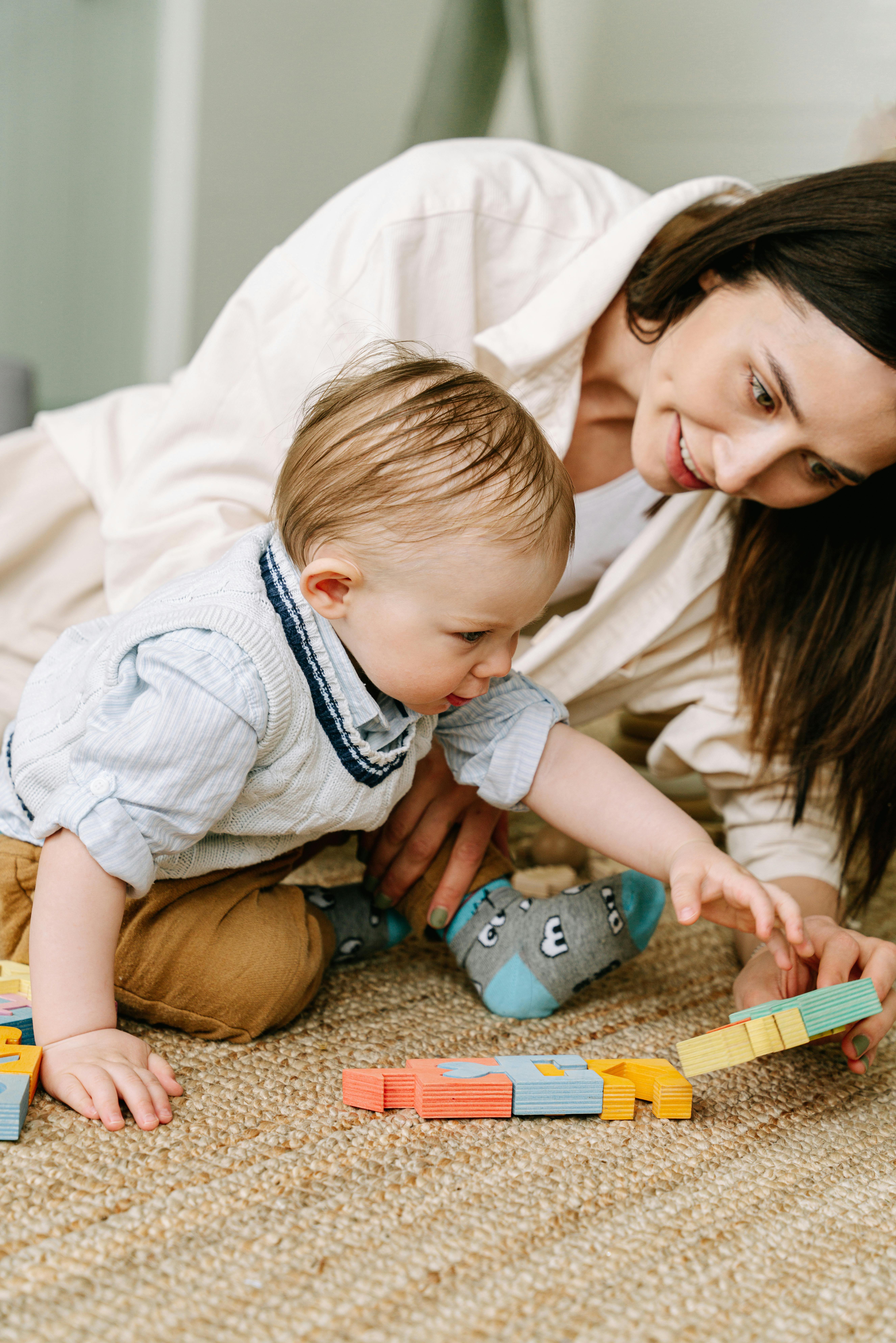 A mother and baby enjoying playtime with colorful building blocks on the carpet indoors.
