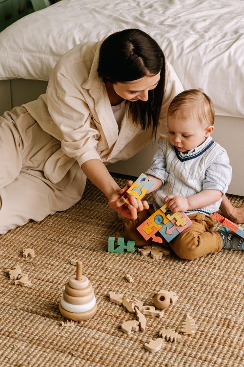 Free Mother and child enjoy bonding time playing with a colorful wooden puzzle on a cozy rug. Stock Photo