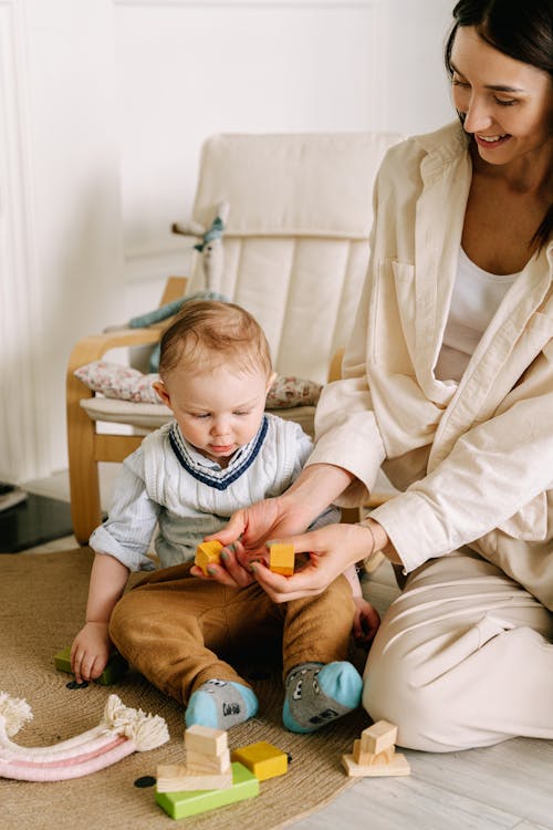 Free Woman in White Dress Shirt Playing with Wooden Blocks Beside Her Baby Stock Photo